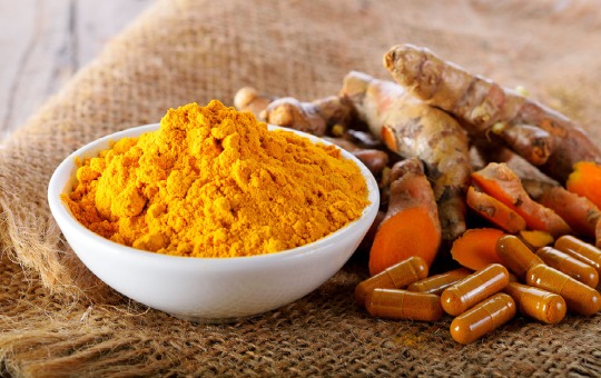 Turmeric with capsules of curcumin and a bowl of powdered curcumin.